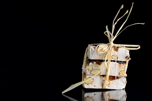 Several pieces of torrone or white nougat with nuts, candied fruits and chocolate are tied together with raffia and lie on a reflective surface in front of a dark background photo