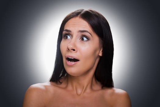 Feeling terrified. Portrait of shocked young shirtless woman looking away and keeping mouth open while standing against grey background photo