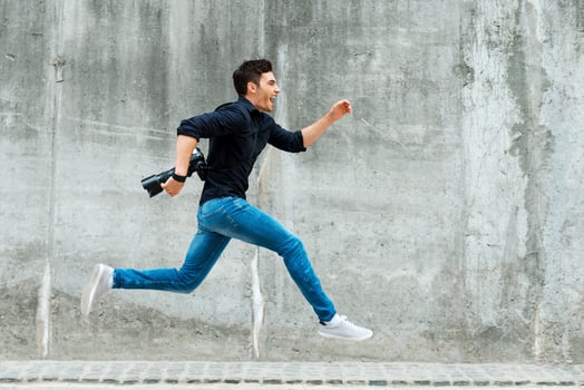Hurrying to be first. Full length of young photographer running against a concrete wall photo