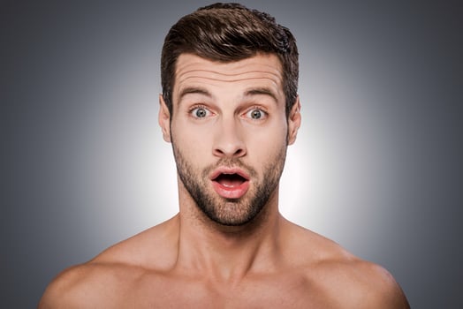 Unbelievable Portrait of surprised young shirtless man looking at camera and keeping mouth open while standing against grey background photo