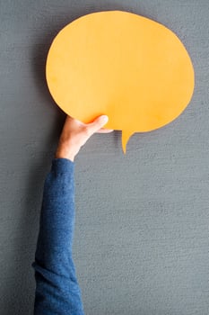 Speech bubble. Close-up of man stretching out empty speech bubble against grey background photo