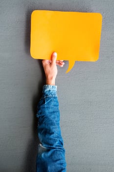 Write your thoughts. Close-up of man stretching out empty speech bubble against grey background photo