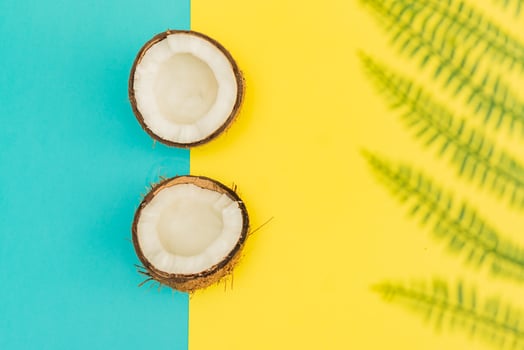 Halves of fresh raw coconut on yellow and blue backgound. Top view, flat lay photo
