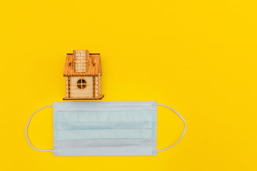protective medical mask and wooden house on yellow background. Stay home, social isolation, coronavirus prevention concept. photo