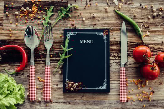 Restaurant menu. Top view of chalkboard menu laying on the rustic wooden desk with vegetables around photo