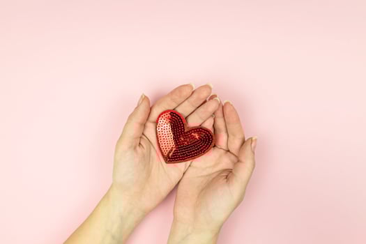 Female hands holding red sequin heart on pink background. Creative minimal layout with copy space photo