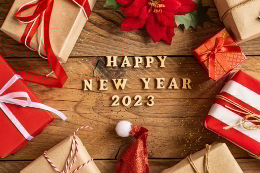 happy new year 2023 festive background with wooden letters and craft gift boxes, poinsettia and santa hat on wooden background. photo