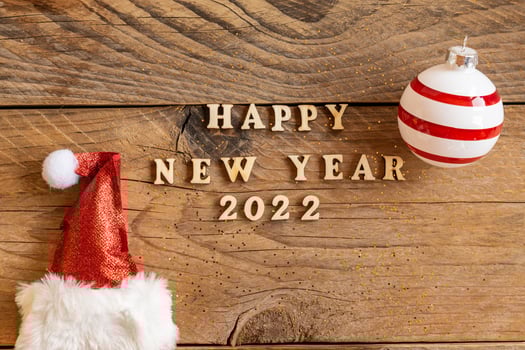 Happy new year 2022 wooden letters quote with red sparkling santa hat and striped bauble on wooden table. Festive greeting card for a new year celebration photo