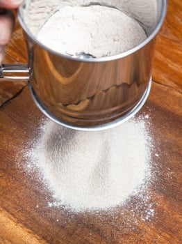 sifting the flour through steel sieve on board photo