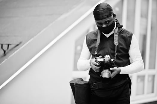 Young professional african american videographer holding professional camera with pro equipment. Afro cameraman wearing black duraq and face protect mask, making a videos. photo