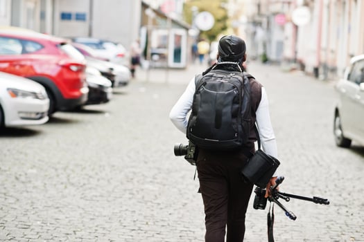 Young professional african american videographer holding professional camera with tripod pro equipment. Afro cameraman wearing black duraq making a videos. photo