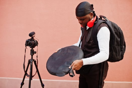 Young professional african american videographer holding professional camera with pro equipment. Afro cameraman wearing black duraq making a videos. photo