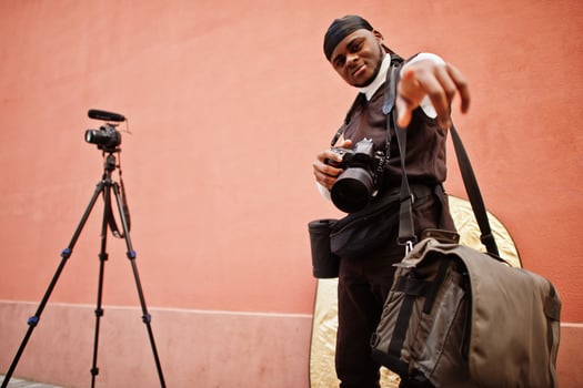 Young professional african american videographer holding professional camera with pro equipment. Afro cameraman wearing black duraq making a videos. photo