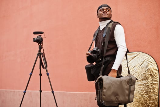 Young professional african american videographer holding professional camera with pro equipment. Afro cameraman wearing black duraq making a videos. photo