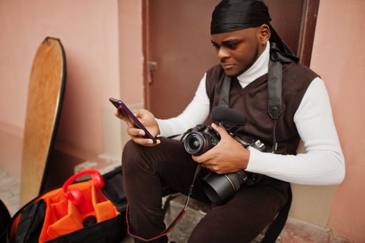 Young professional african american videographer holding professional camera with pro equipment. Afro cameraman wearing black duraq making a videos. photo