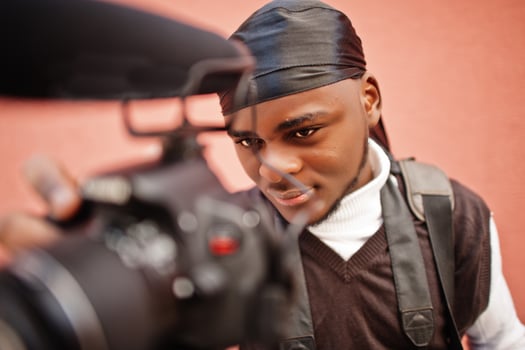 Young professional african american videographer holding professional camera with pro equipment. Afro cameraman wearing black duraq making a videos. photo