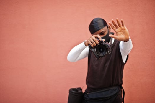 Young professional african american videographer holding professional camera with pro equipment. Afro cameraman wearing black duraq and face protect mask, making a videos. photo