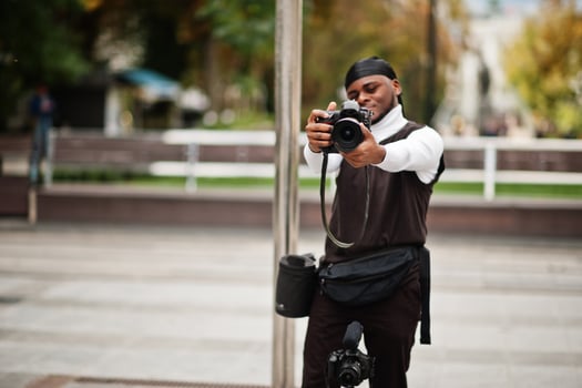 Young professional african american videographer holding professional camera with pro equipment. Afro cameraman wearing black duraq making a videos. photo