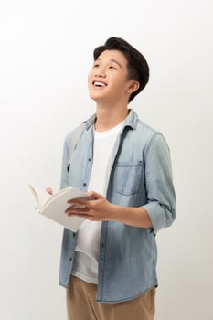 A young Asian man standing in a blue shirt, holding a book and reading, isolated for white background. photo