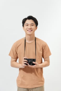 Confident photographer. Handsome young man holding digital camera and smiling while standing against white background photo