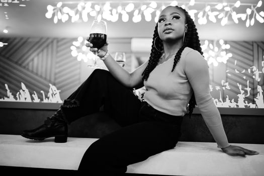 Portrait of attractive young african american woman wearing in green sweater and black jeans pose at restaurant with glass of red wine at hand. photo