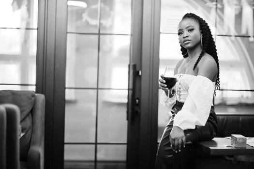 Beautiful african american woman in white blouse and red leather pants pose at restaurant with glass of wine. photo