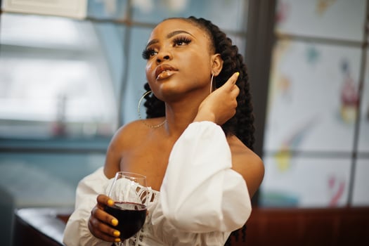 Beautiful african american woman in white blouse and red leather pants pose at restaurant with glass of wine. photo