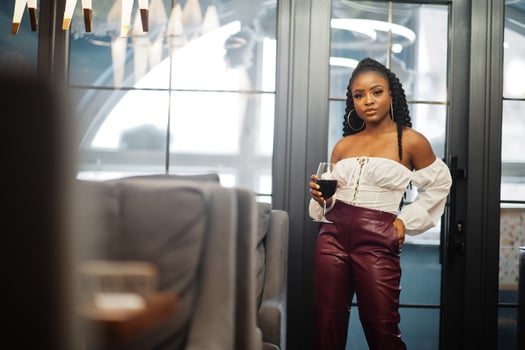 Beautiful african american woman in white blouse and red leather pants pose at restaurant with glass of wine. photo
