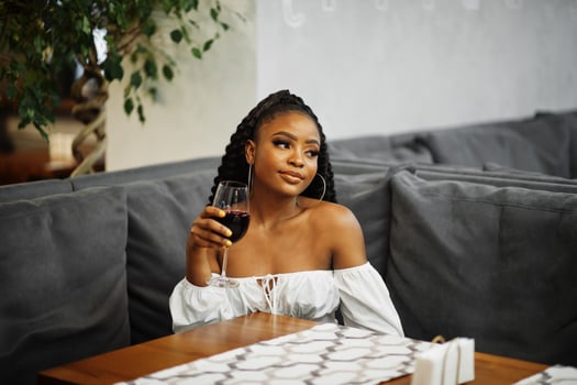 Beautiful african american woman in white blouse and red leather pants pose at restaurant with glass of wine. photo