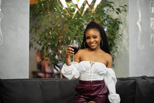 Beautiful african american woman in white blouse and red leather pants pose at restaurant with glass of wine. photo