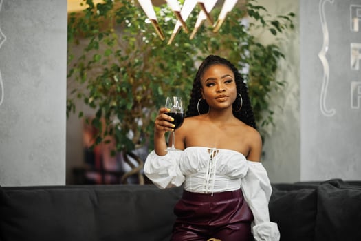 Beautiful african american woman in white blouse and red leather pants pose at restaurant with glass of wine. photo