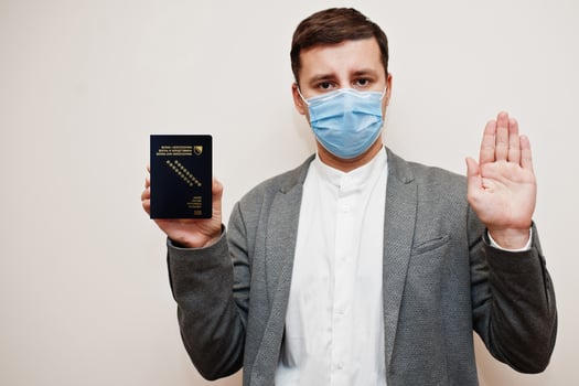 European man in formal wear and face mask, show Bosnia and Herzegovina passport with stop sign hand. Coronavirus lockdown in Europe country concept. photo