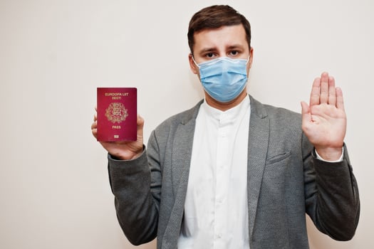 European man in formal wear and face mask, show Estonia passport with stop sign hand. Coronavirus lockdown in Europe country concept. photo