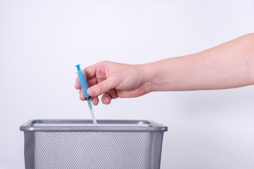 A hand tosses a used syringe in the trash on a gray background. photo