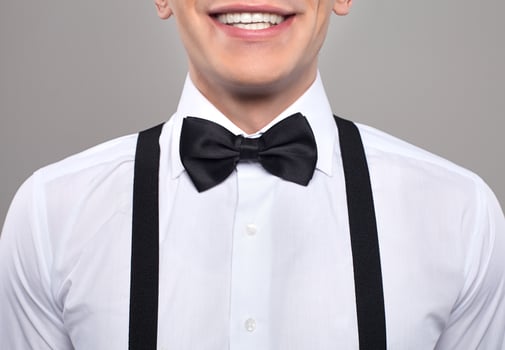 Close-up on nerd. Cropped image of young nerd man in bow tie and suspenders smiling while standing against grey background photo
