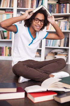 I love studying. Cheerful African teenager holding book on head and smiling while sitting on the floor at the library photo