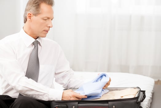 Preparing for business trip. Confident grey hair man in shirt and tie packing his luggage while sitting on the bed photo