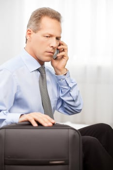 Confident executive. Serious grey hair man in shirt and tie talking on the phone while sitting on bed photo