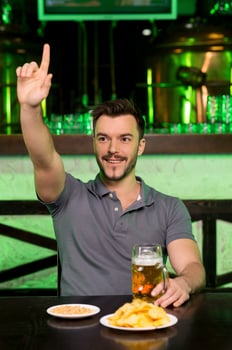 Waiter  Cheerful young man raising up hand while sitting in bar photo