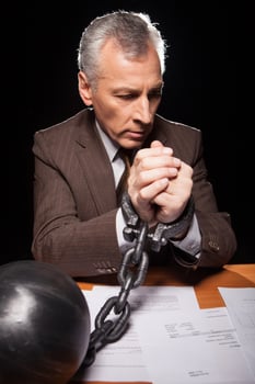 Chained businessman. Frustrated senior man in formalwear sitting at his working place and looking at camera while isolated on black background photo