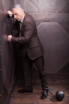 Chained businessman. Full length of grey hair senior man in formalwear with the shackles on his leg leaning at the wall photo