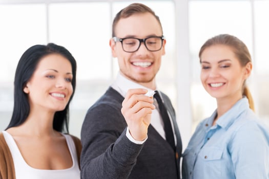 Coming up with a strategy. A manager writing something on a glass wall while his employees look on it with smile photo