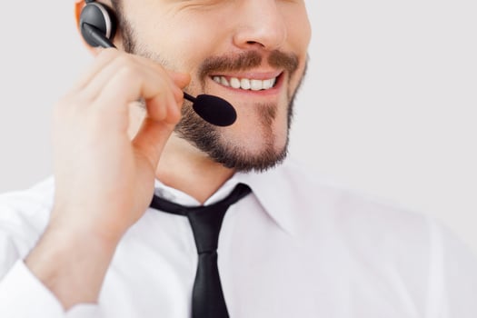 How may I help you Cropped image of handsome young man in formalwear adjusting his headset and smiling while standing against grey background photo