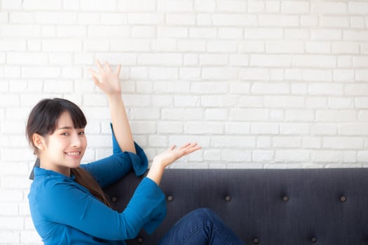 Beautiful young asian woman sitting and smiling happy and presenting something on sofa showing future or planning with message of you, girl cheerful and relax on couch at home, lifestyle concept. photo