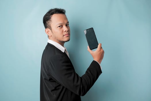 A young Asian businessman in a black suit feels serious and focus holding a smartphone and showing the copy space on its screen in hand. photo