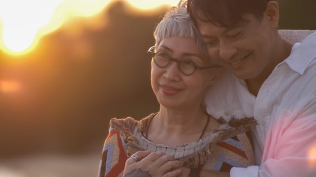Asian retired couple relaxing by the sea in summer. A senior man taking care to his partner while standing on the beach photo
