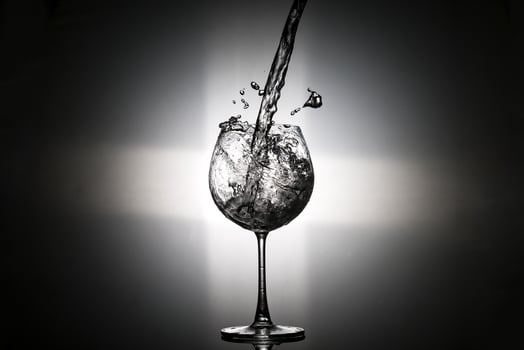 Pouring water in to the wine glass with rear light on black background photo