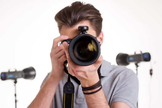 Smile to the camera Young man in polo shirt shooting you with digital camera while standing in studio with lighting equipment on background photo