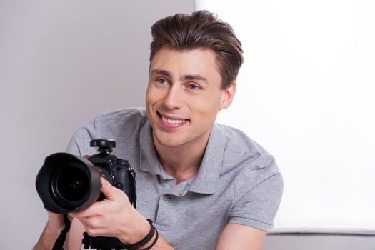 Photographer at work. Young man in polo shirt holding digital camera and looking away while standing in studio with lighting equipment on background Photographer at work. Young man in polo shirt holding digital camera and looking away while standing in st photo