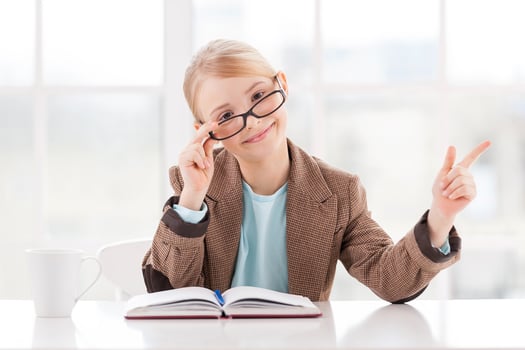 Look at that Cheerful little girl in glasses and formalwear sitting at the table and pointing away photo